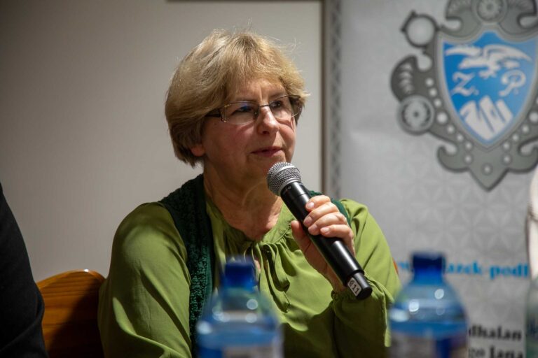 a woman speaking into a microphone in front of a group of people sitting in chairs